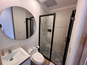Une salle de bain comprenant des toilettes, un lavabo, un miroir, une douche et un sol carrelé.