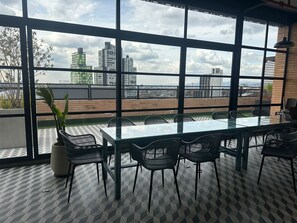 Une salle de conférence dotée d’une table et de chaises en verre, de grandes fenêtres offrant une vue sur la ville et d’une plante en pot.