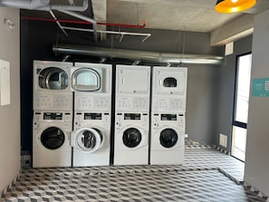 A laundry facility with multiple washing machines, a tiled floor, and visible pipes on the ceiling.