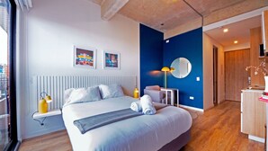 A modern hotel room with a large bed, a bedside lamp, a small table, a chair, a mirror, and artwork on the wall. - U-GO Edificio Next Living Bogota (Bogotá)