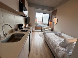 A compact hotel room with a kitchenette, a bed, a seating area, and a large window offering a city view. - U-GO Edificio Next Living Bogota (Bogotá)