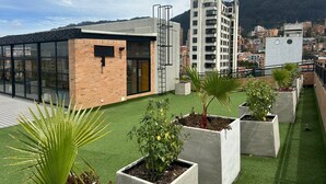 Eine Dachterrasse mit künstlichem Rasen, Betonpflanzgefäßen mit Bepflanzung und einem modernen Gebäude mit großen Fenstern und einer Ziegelaußenwand.