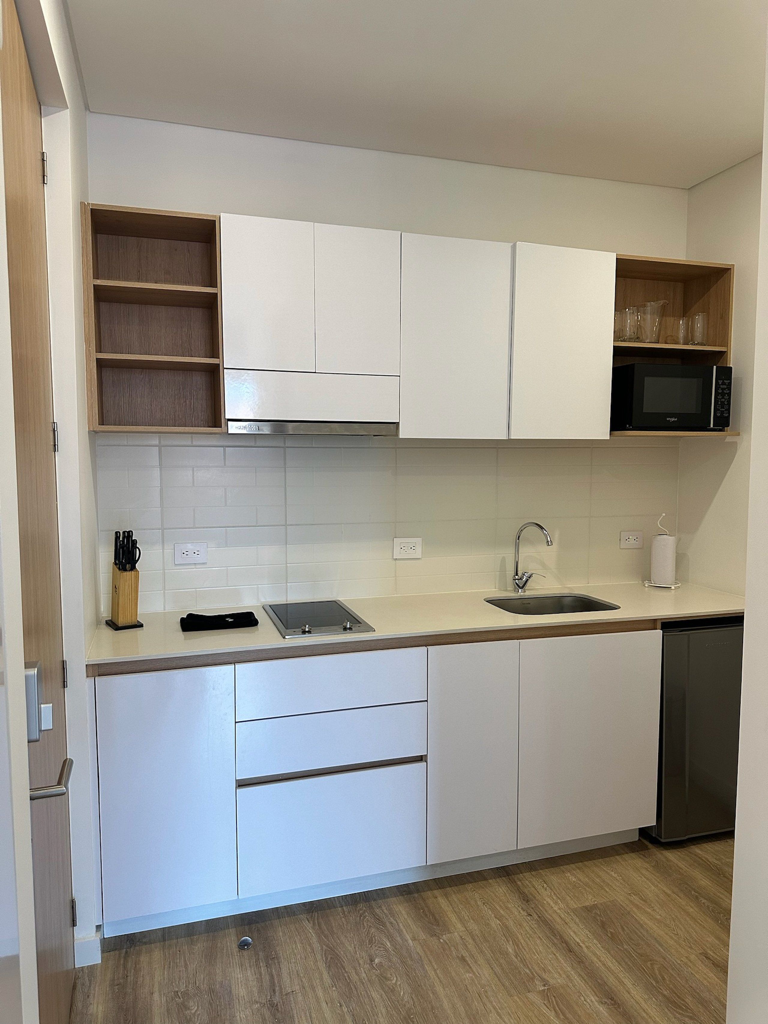 A modern kitchen with white cabinets, a built-in microwave, a sink, and a countertop with a knife block and a tablet.