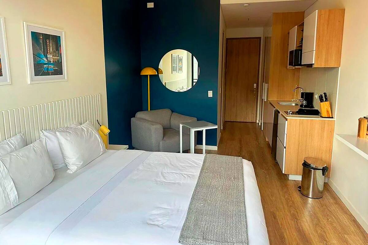 Une chambre d’hôtel équipée d’un lit, d’un bureau, d’un miroir, d’une kitchenette et d’une salle de bain.