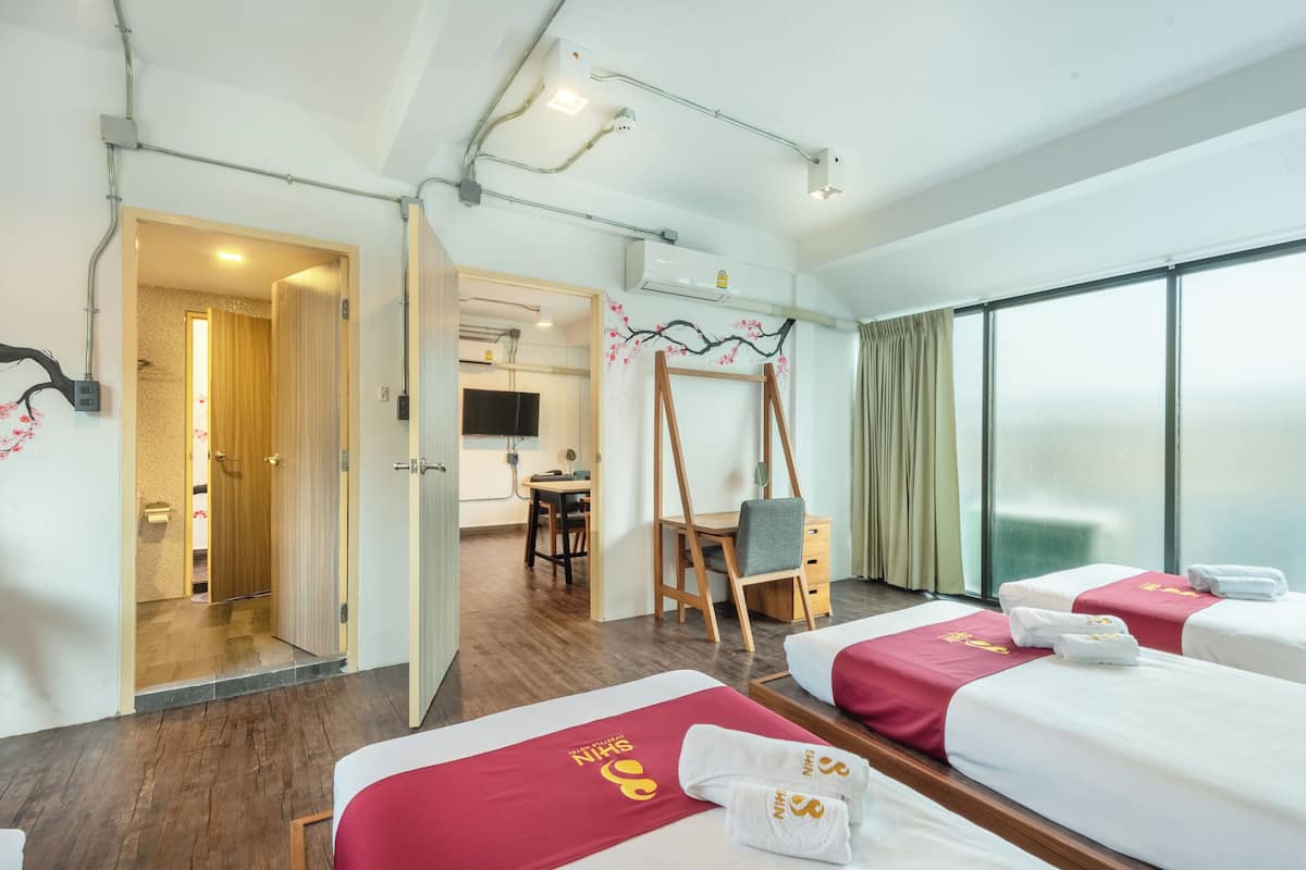 Habitació d'hotel amb dos llits, una taula de treball, una cadira i zona de dutxa.