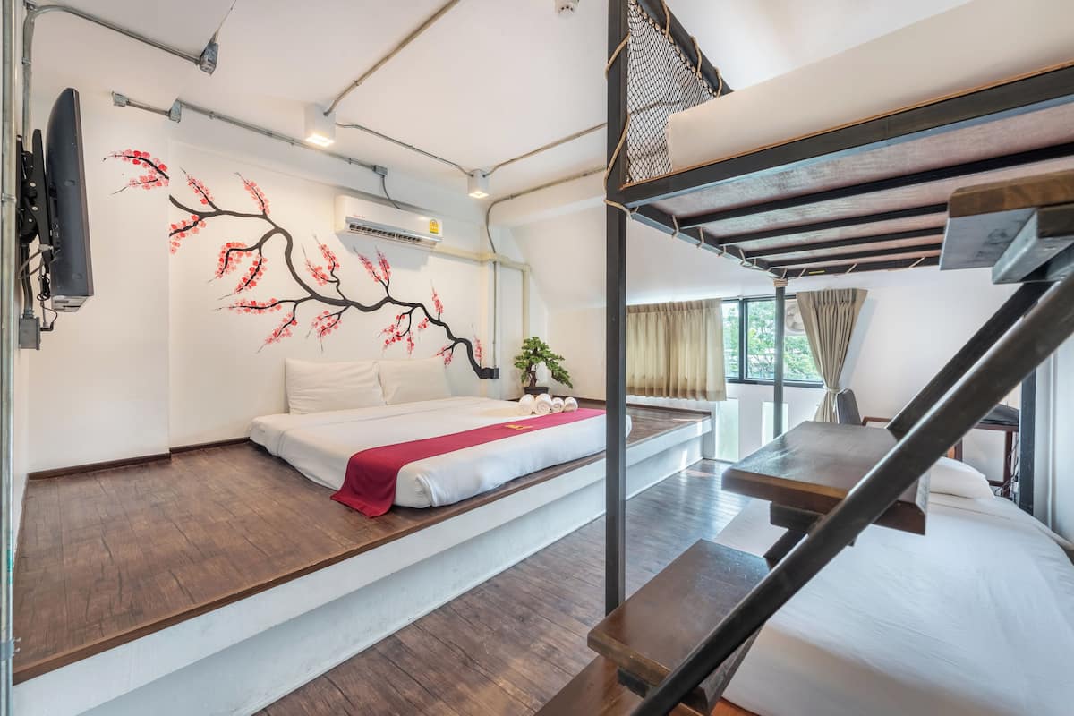 Habitació d'hotel moderna amb un llit, una paret decorativa vermella, una escala i una finestra amb cortines.