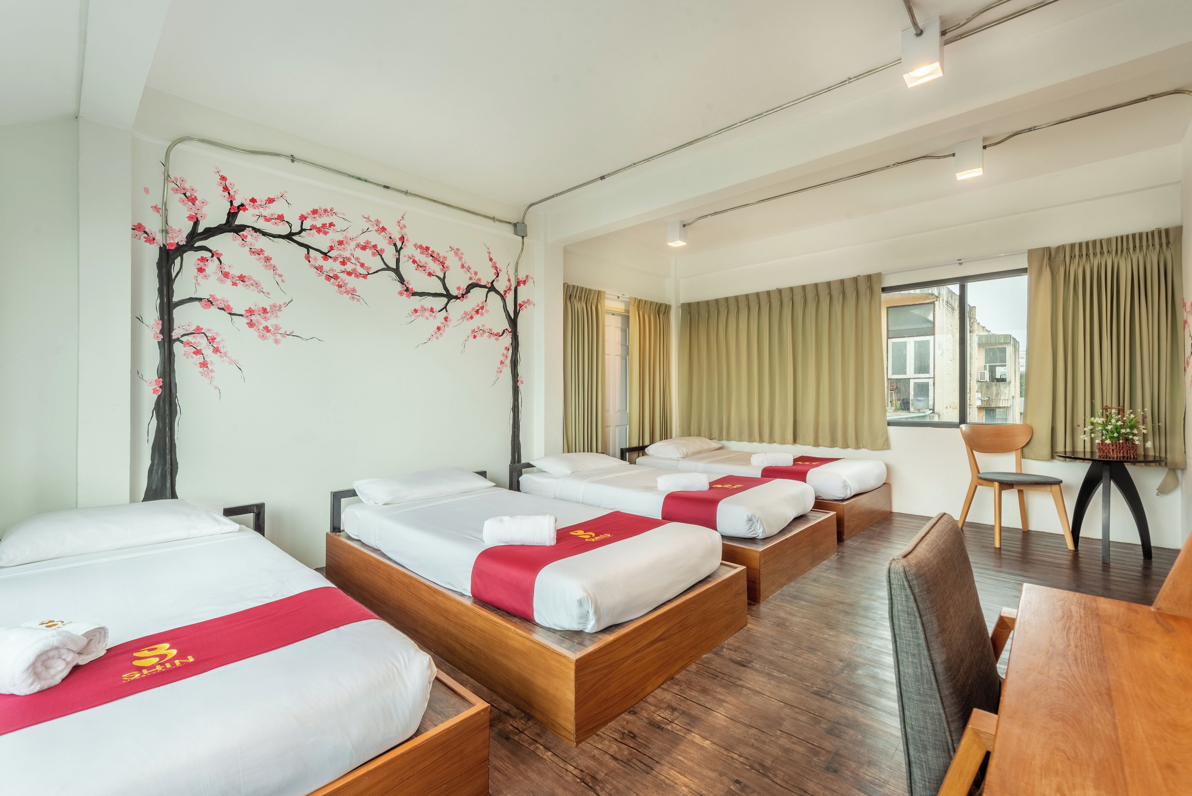 A hotel room with four beds, a dining area, and a large window with curtains.