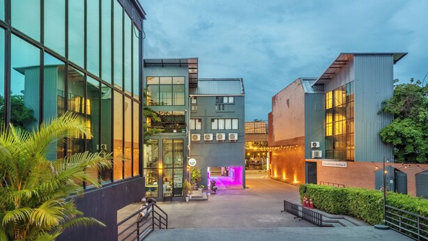 Ein modernes Gebäude mit großen Fenstern, einer beleuchteten Neon-Eingangspartei und einem gepflegten Außenbereich mit Pflanzen.