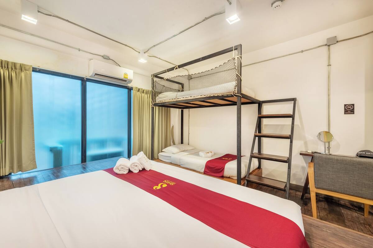 Habitació d'hotel amb un llit superposat, un escriptori amb una cadira, un mirall i una finestra amb cortines.