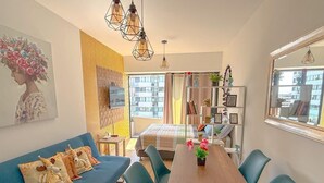 A modern living room with a sofa, dining table, chairs, a bed, and a large window with a city view. - Exclusive Apartment Just Steps from San Isidro (Lince)