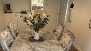 Une salle à manger avec une table en marbre, des chaises rembourrées et un vase rempli de fleurs.