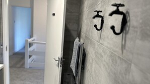 Un couloir avec un sol carrelé, une serviette suspendue à un porte-serviettes et une porte donnant sur une autre pièce.