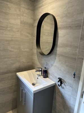 Une salle de bain avec un lavabo blanc, un miroir ovale noir et un flacon de savon pour les mains.