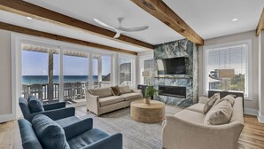 A spacious living room with a large window overlooking the ocean, a fireplace, and modern furniture. - The Turtle's Palace- Oceanfront - Pool - Hot Tub - Dog Friendly (Surf City)