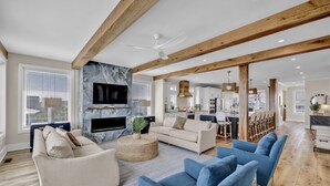 A spacious living room with a fireplace, a large TV, and a kitchen in the background. - The Turtle's Palace- Oceanfront - Pool - Hot Tub - Dog Friendly (Surf City)