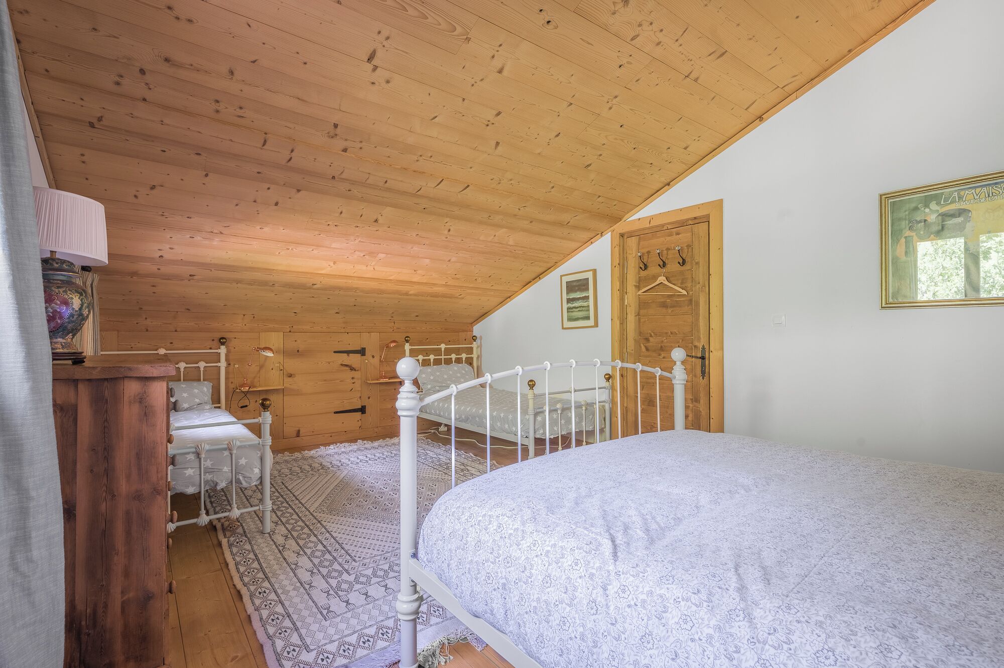 Une chambre avec un plafond en bois, un lit, une commode et une porte.