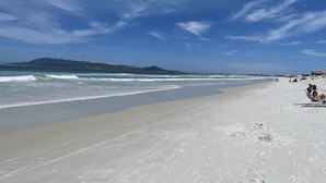 A beach with a clear sky, waves, and footprints in the sand.