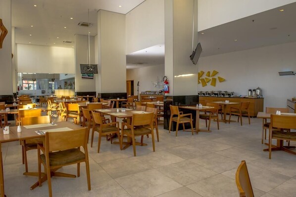 Un grand espace dédié à la salle à manger, avec des tables et des chaises en bois, une cuisine à l’arrière-plan et un mur orné d’un logo jaune.
