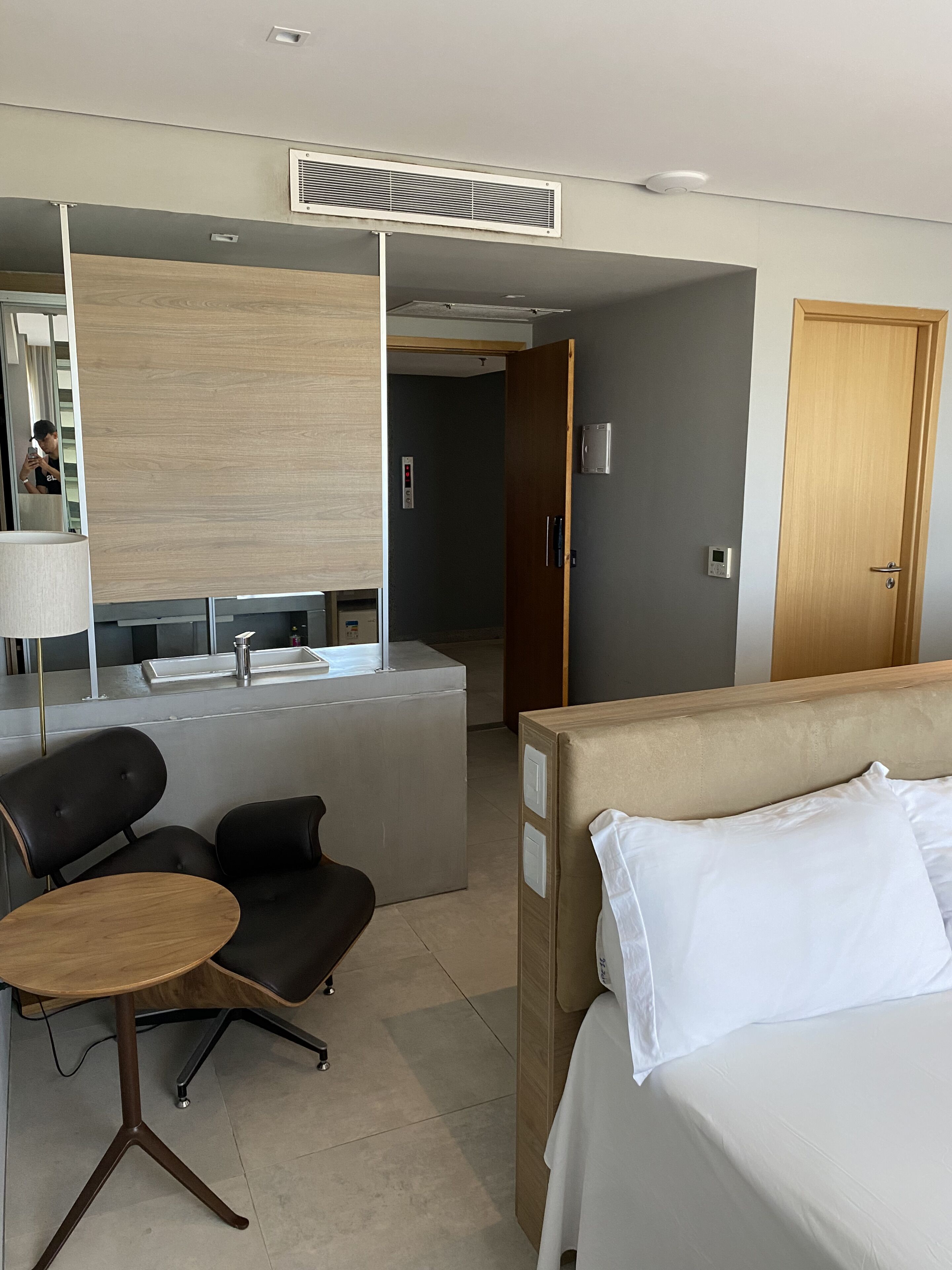 Una habitación de hotel con cama, un escritorio con silla, un espejo y una kitchenette.