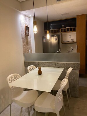 A modern kitchen with a white table and chairs, a refrigerator, and pendant lights. - Paiva Home Stay by Flatbpaiva (Jaboatão dos Guararapes)