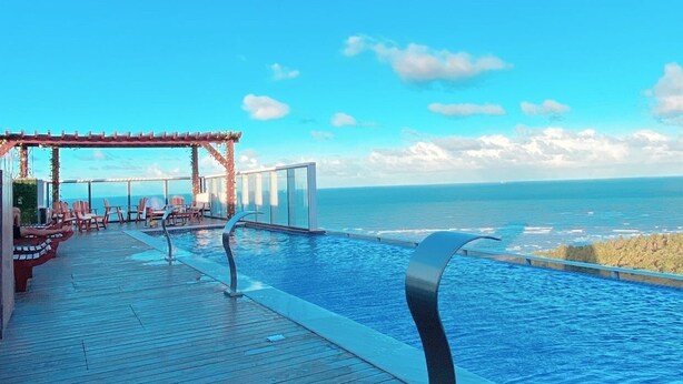 A poolside area with a wooden deck, lounge chairs, and a view of the ocean.