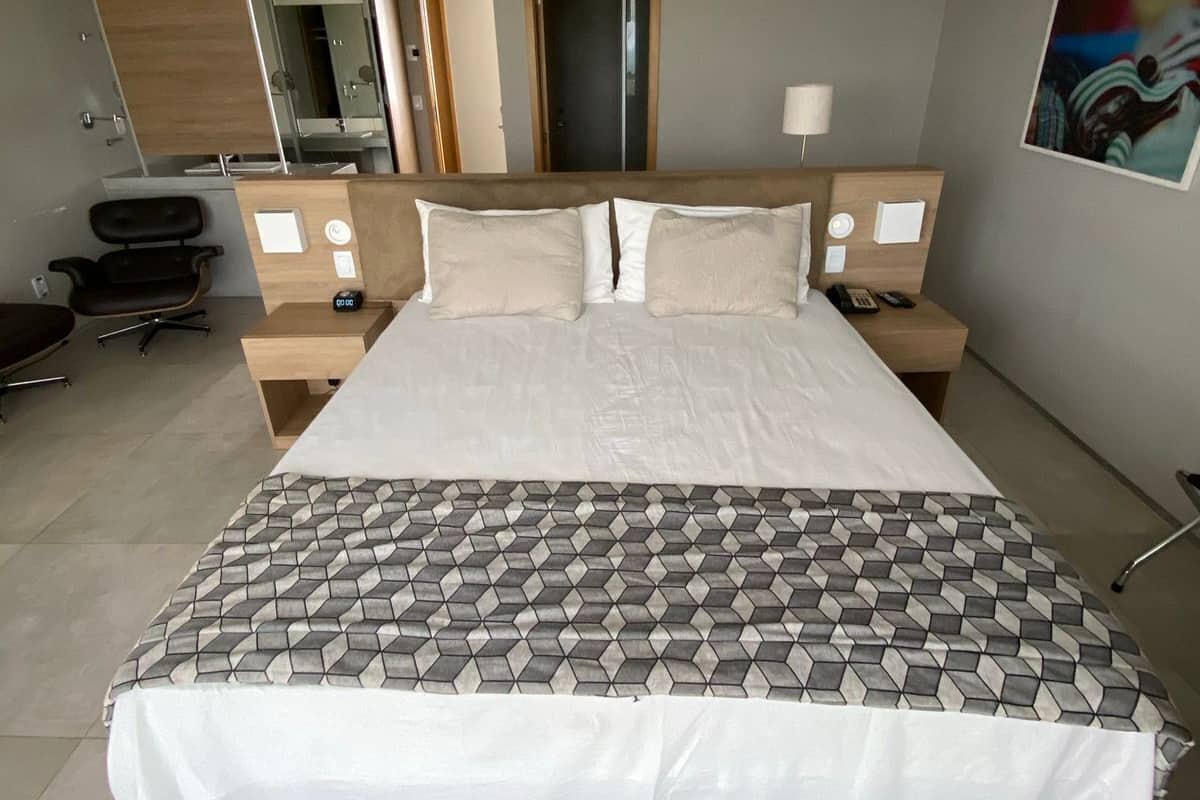 A modern hotel bedroom with a large bed, bedside tables, a desk, and a chair.
