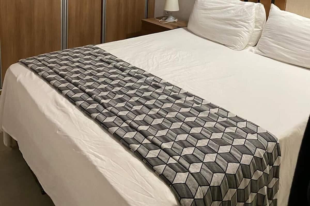 A hotel room with a bed, a nightstand, a lamp, and a picture of the Eiffel Tower on the wall.