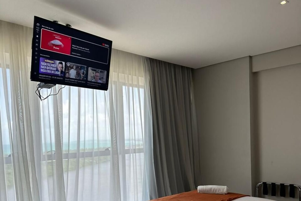 Een hotelkamer met twee bedden, een aan de muur bevestigde televisie en een raam met gordijnen.