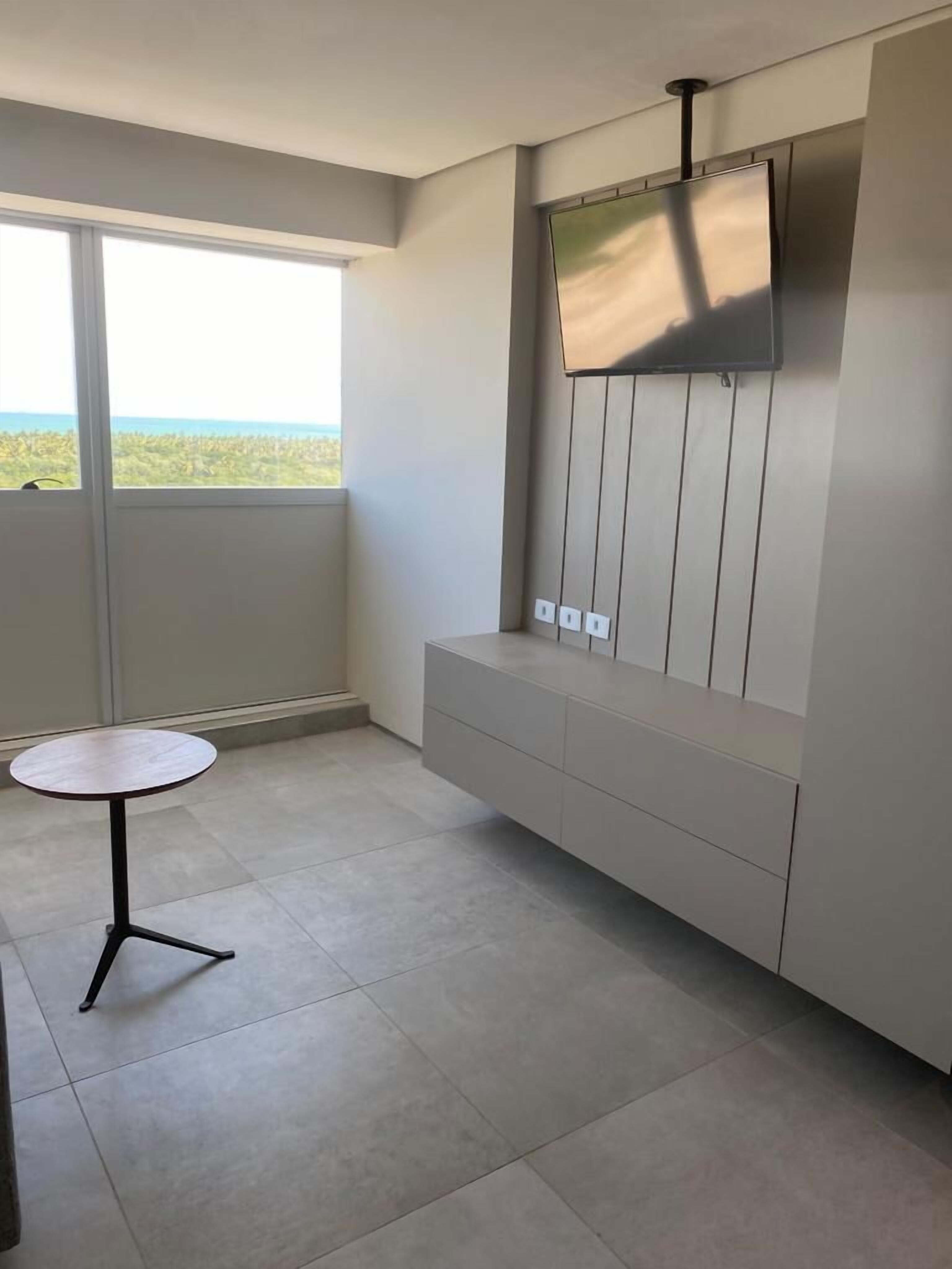 A modern room with a built-in TV, a small round table, and a view of the ocean through a large window.