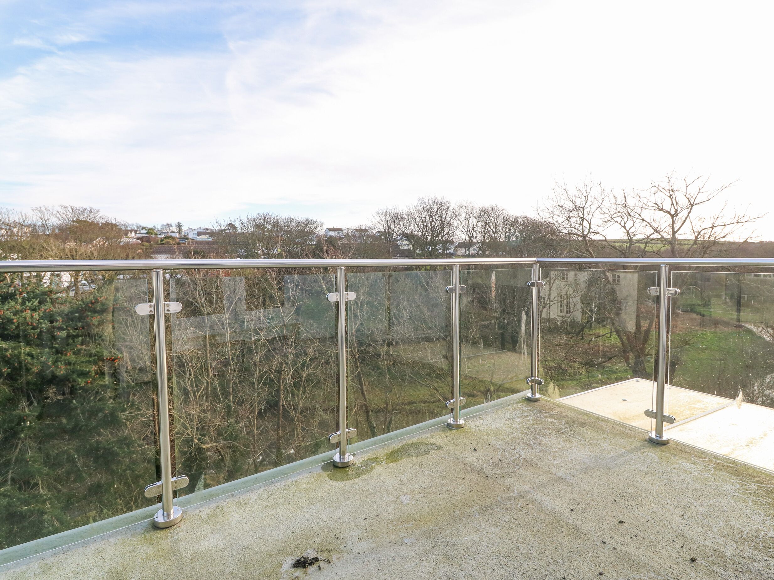 A balcony with a glass railing overlooking a landscape with trees and buildings.