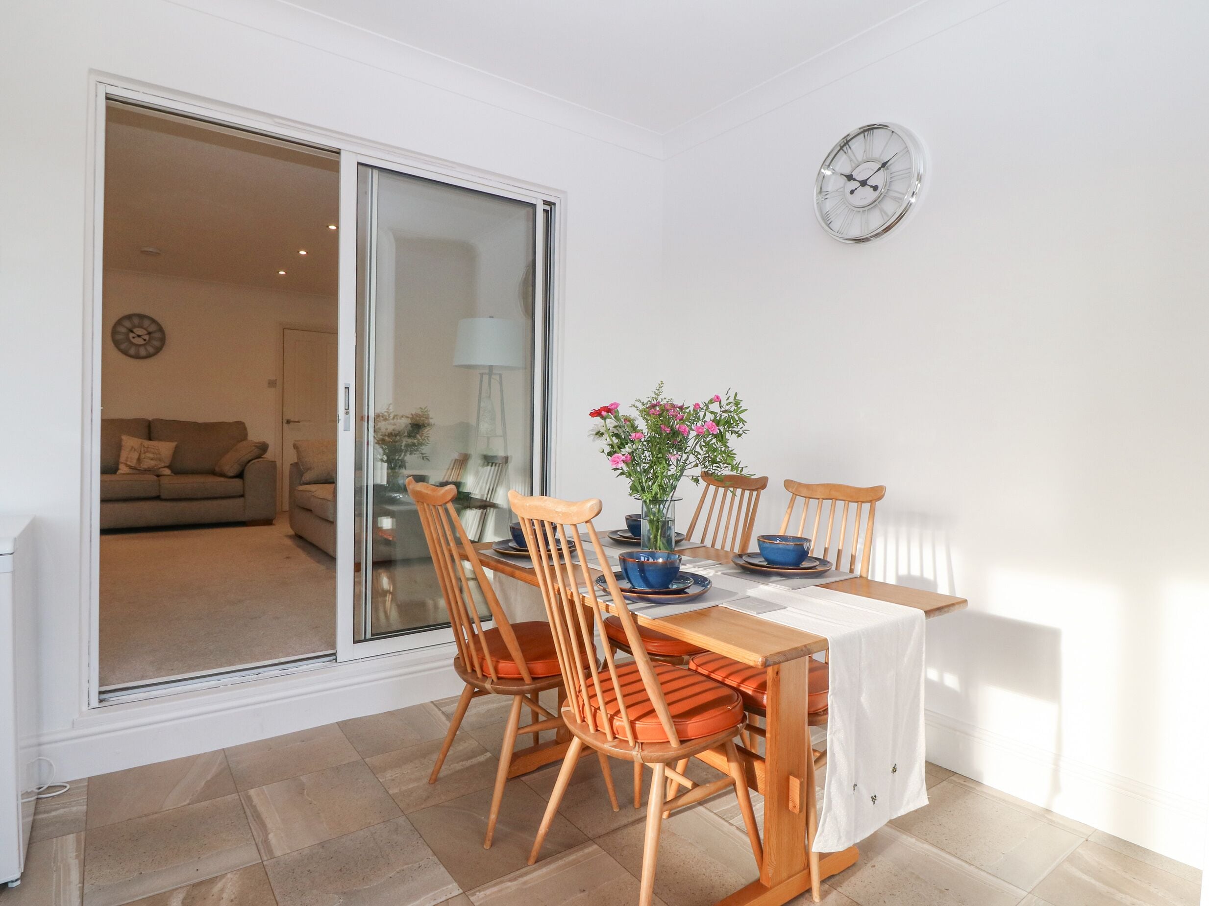 A dining area with a table, chairs, a vase with flowers, and a clock on the wall.