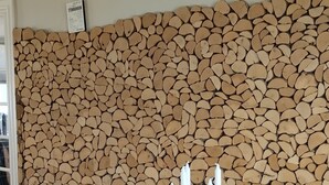 Un comedor con una mesa cubierta con mantel floral, cuatro velas blancas y un montón de leña apoyada contra la pared.