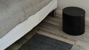 Un dormitorio con una cama, un objeto cilíndrico negro en el suelo y una obra de arte enmarcada en la pared.
