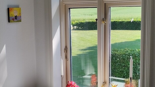 Una habitación con un escritorio blanco, una silla y un ventanal con vistas a un campo verde.