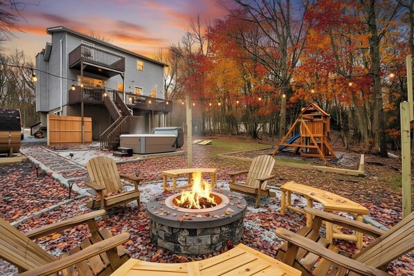 A backyard with a fire pit, outdoor seating, a wooden playhouse, and a staircase leading to a deck.