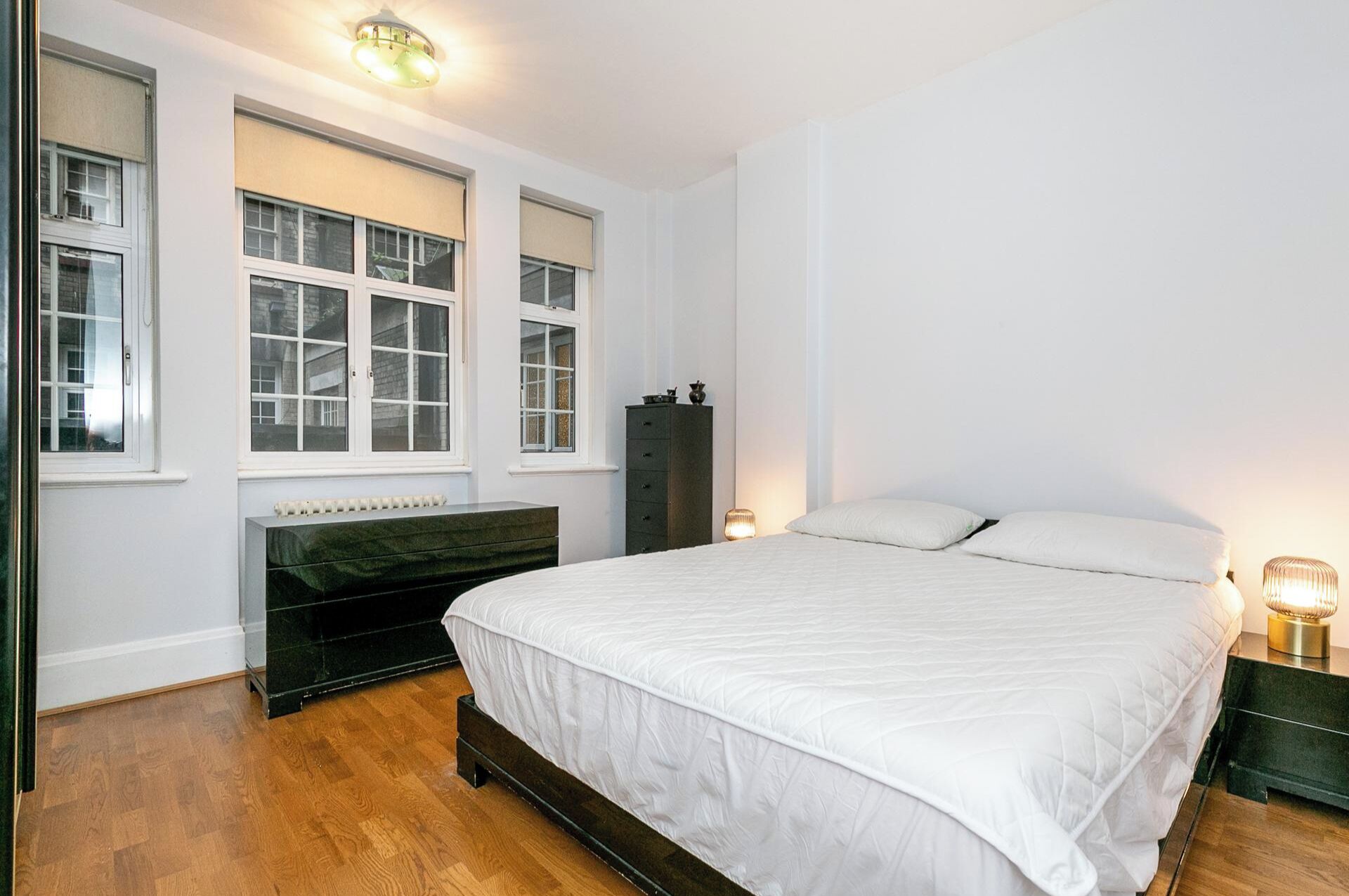 Een slaapkamer met een groot bed, een dressoir, een radiator en drie ramen.