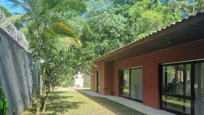 A building with a red exterior, large windows, and a pathway leading to a door. - Casa em Maresias em Meio a Mata (Praia de Maresias São Sebastião)
