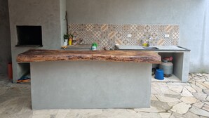 A kitchen with a large island, tiled backsplash, and a stone floor. - Casa em Maresias em Meio a Mata (Praia de Maresias São Sebastião)