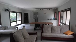 A modern living room with a sofa, a dining table, and a kitchen in the background. - Casa em Maresias em Meio a Mata (Praia de Maresias São Sebastião)
