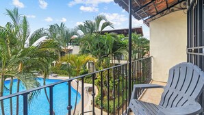 Un balcon avec une piscine, entouré de palmiers et offrant une vue sur un immeuble.