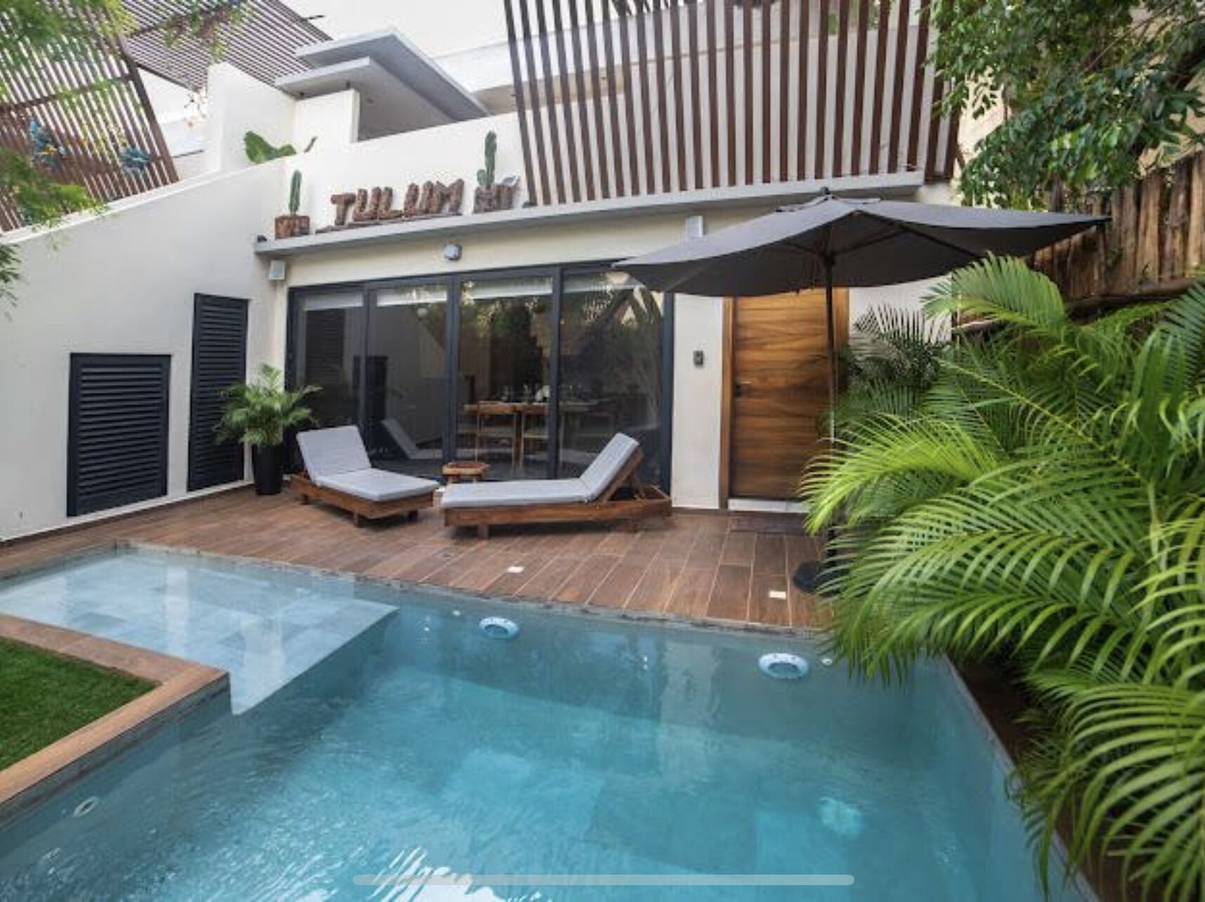 Un área de piscina moderna al aire libre con dos sillones de descanso y una terraza de madera.