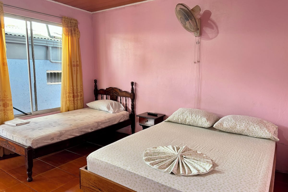 A bedroom with two beds, a wall-mounted fan, and a window with curtains.