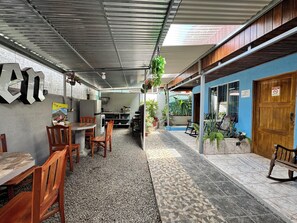 A covered outdoor dining area with tables and chairs, a kitchen in the background, and potted plants. - Cabinas Las Palmas (La Fortuna)
