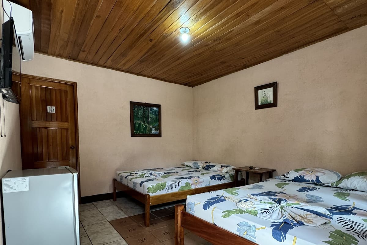 A room with two wooden beds, a small table, a refrigerator, and a wooden cabinet.