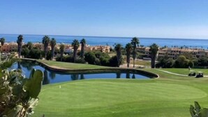 A golf course with a pond, palm trees, and a view of the sea.