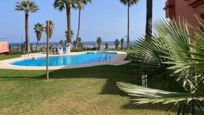 A swimming pool surrounded by palm trees and a building with a red facade.