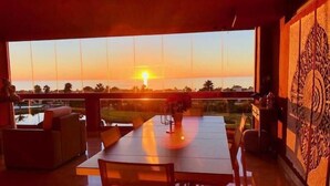 A dining area with a view of the sunset over a body of water, a large window, and a decorative wall panel.