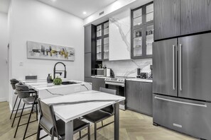 A modern kitchen with a marble countertop, stainless steel appliances, and a dining area with bar stools.