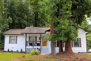 A white house with a porch, a large tree in front, and a small garden.