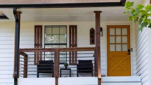 Un bâtiment blanc avec une porte en bois, un petit porche doté d’une balustrade et deux fenêtres avec des volets.